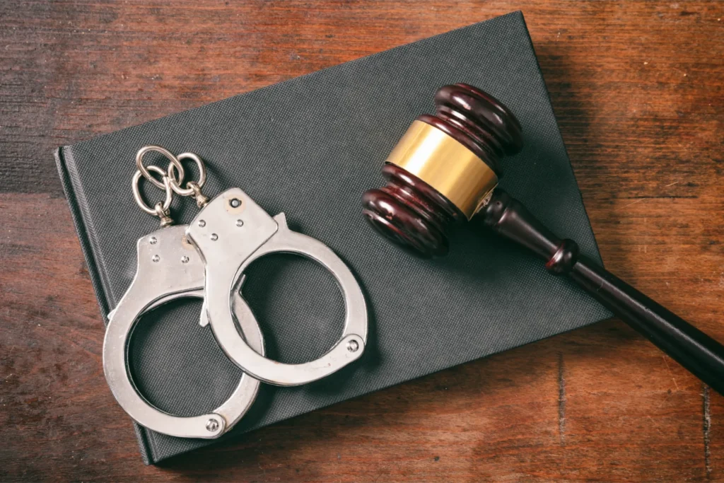 Handcuffs, gavel, and evidence card arranged on dark surface with wooden background