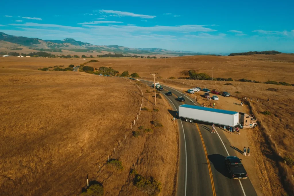Coach bus and cars on rural highway through golden fields under blue sky.