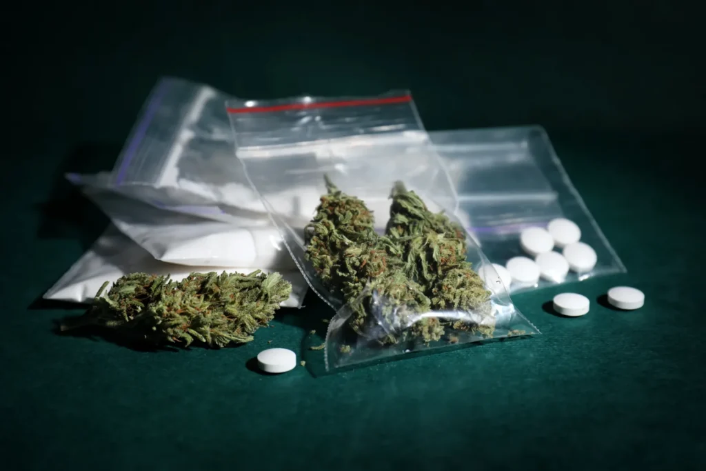 Evidence photo: dried hemp buds and ecstasy pills on dark green tabletop.