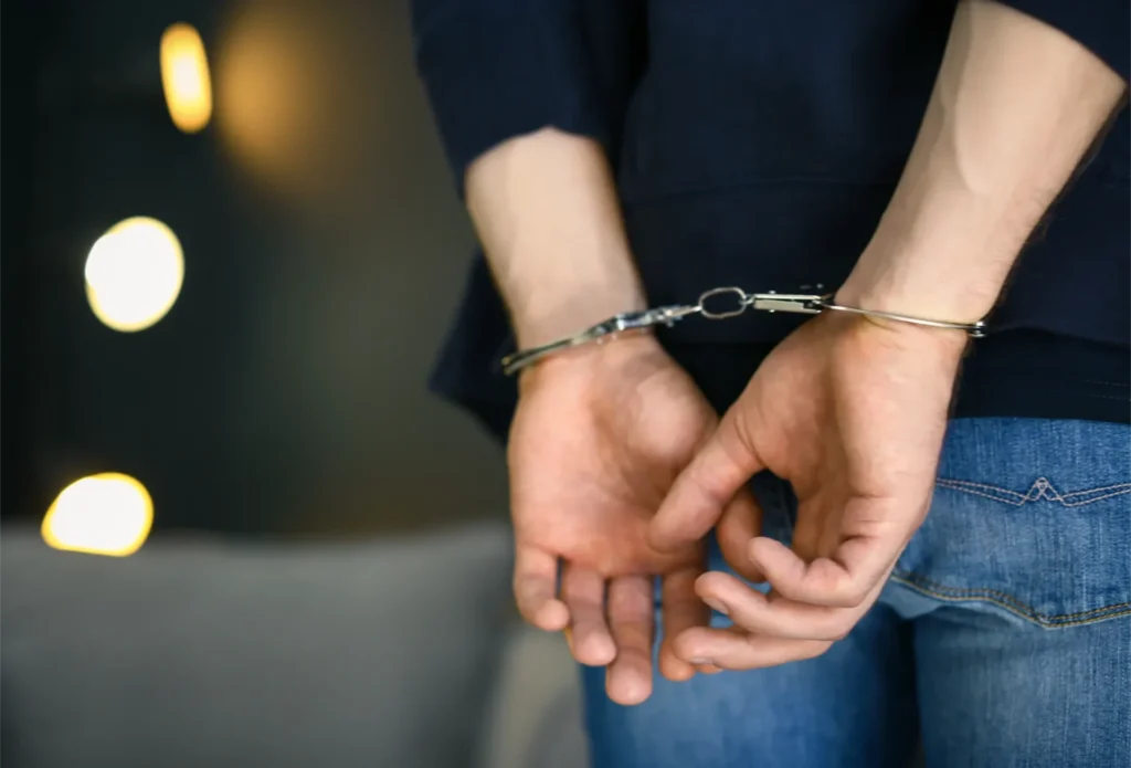 Handcuffed wrists held together indoors under warm bokeh lights, man in custody