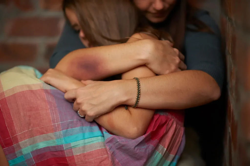 Warm indoor hug between friends, striped and dark clothing in soft, intimate lighting