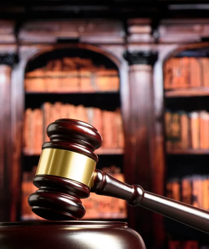 Gavel on judge’s bench with blurred law library books and warm courtroom lighting
