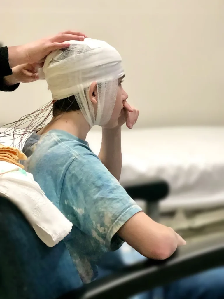 Nurse adjusts disposable head cover on masked healthcare worker before clinic shift
