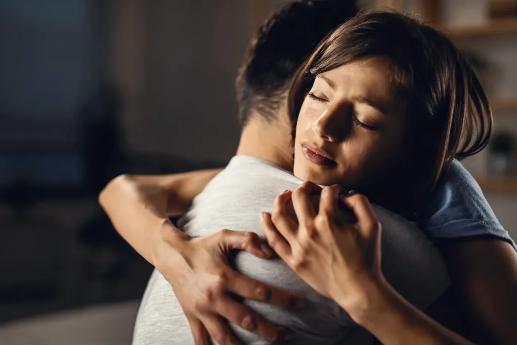 Warm indoor hug, two people comforting each other with tender closeness and relief.
