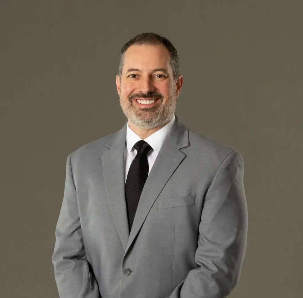 Jay Gerber corporate headshot in light gray suit, dark shirt, black tie studio portrait