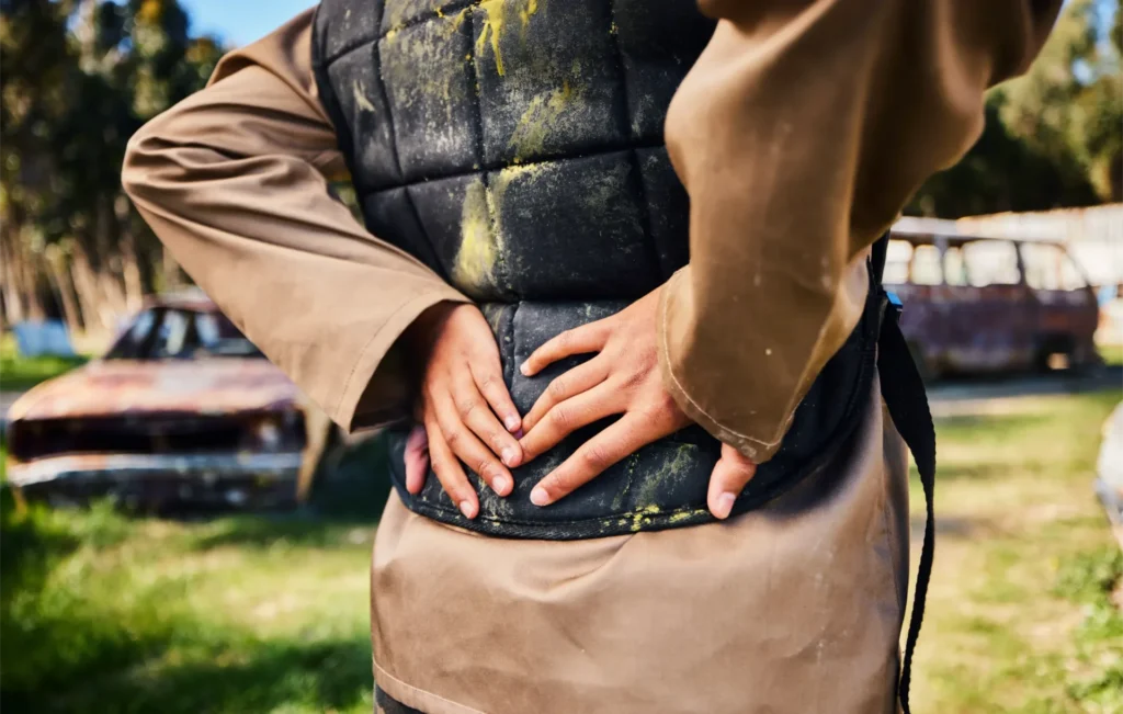 Paintball aftermath: person holds lower back and waist outdoors in daylight