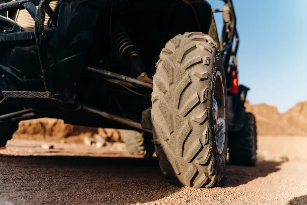 Rugged off-road truck tire close-up with deep tread and suspension in desert sand