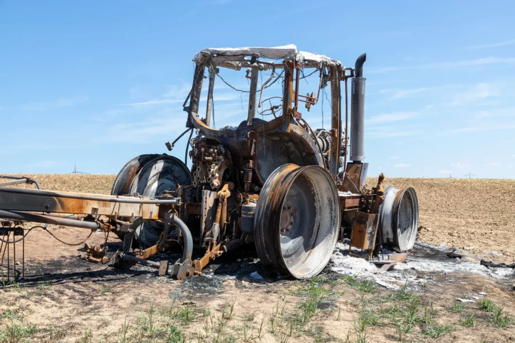 Rusty old tractor parked on dry harvested field under clear blue sky, rural farmland.